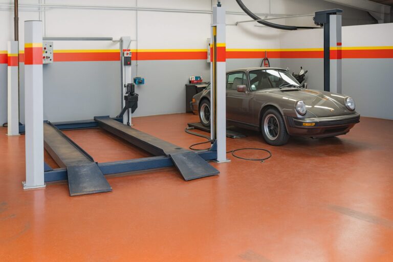 Porsche 911 SC grise sur un pont élévateur dans l'atelier FLAT au sol orange