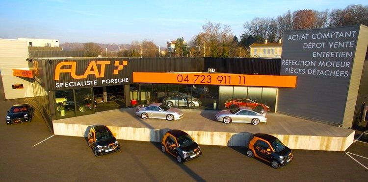 Façade du bâtiment FLAT Spécialiste Porsche en bordure de l'autoroute A7, Porsche et Smart de courtoisie sur le parking