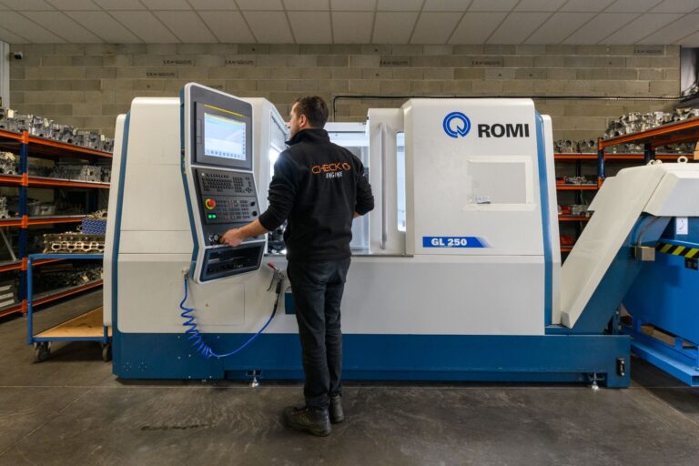 Technicien FLAT pilotant le tour à commande numérique ROMI du centre d'usinage, rayonnages de moteurs en arrière-plan