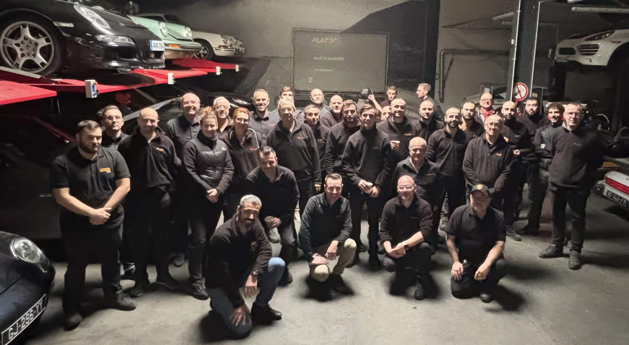 L'équipe de FLAT Porsche Experts réunie dans l'atelier de Sérézin-du-Rhône, Porsche sur ponts élévateurs en arrière-plan