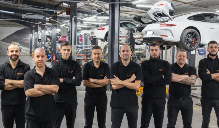Les mécaniciens du service après-vente FLAT bras croisés dans l'atelier, une Porsche 911 GT3 sur pont derrière eux