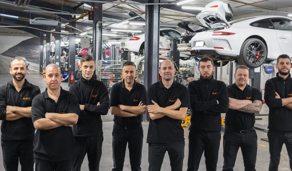 Les mécaniciens du service après-vente FLAT bras croisés dans l'atelier, une Porsche 911 GT3 sur pont derrière eux