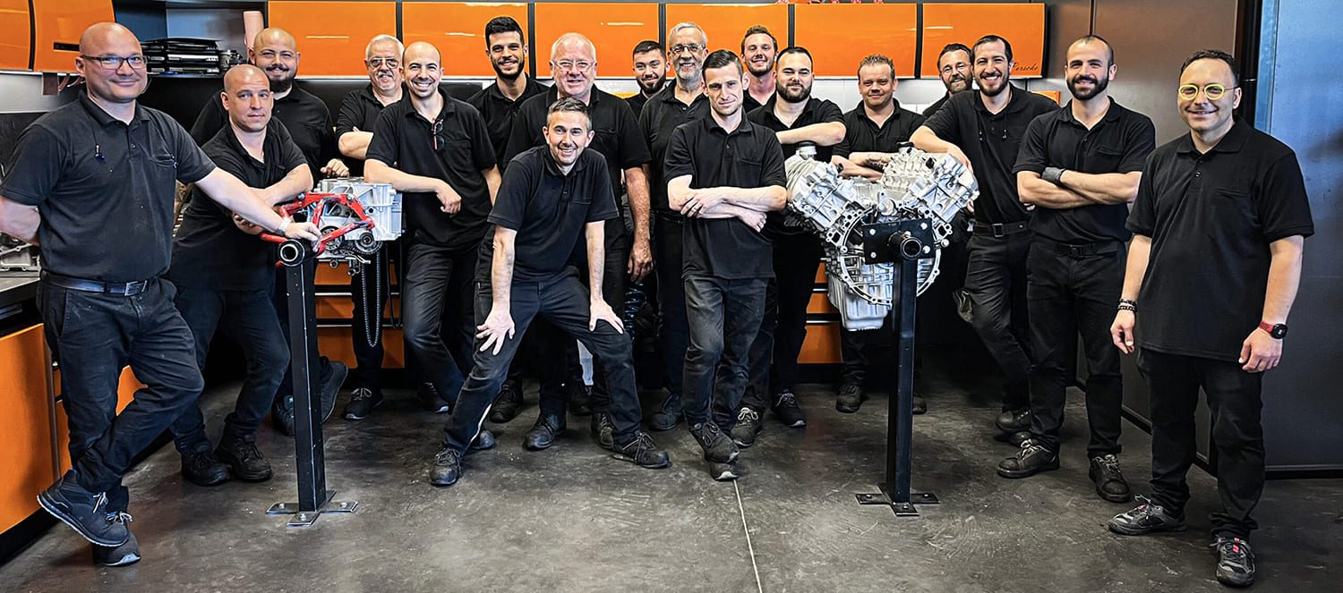 Les techniciens du service production de FLAT autour de moteurs flat-six sur supports, dans l'atelier moteur aux établis orange