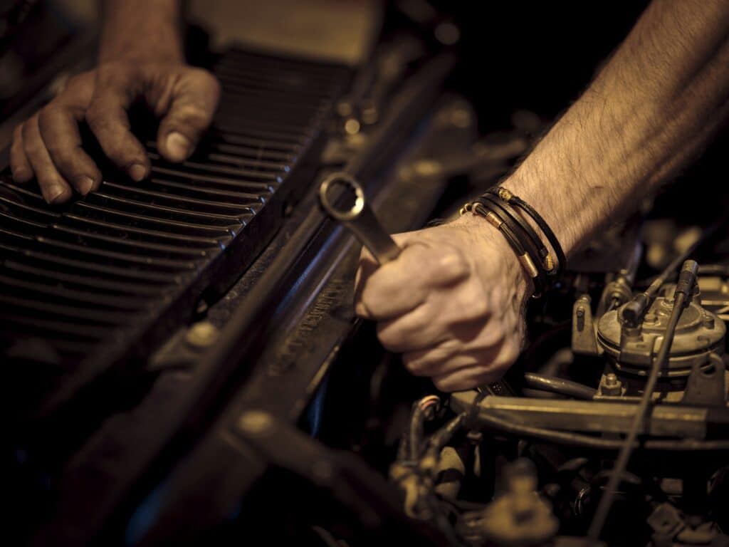 Mains de mécanicien couvertes de cambouis serrant un écrou avec une clé sur un moteur, lumière chaude