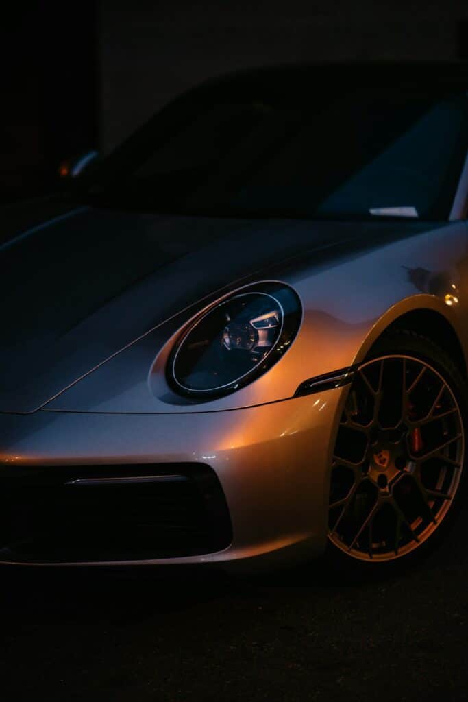 Gros plan sur le phare avant et la jante d'une Porsche 911 type 992 argentée dans la pénombre
