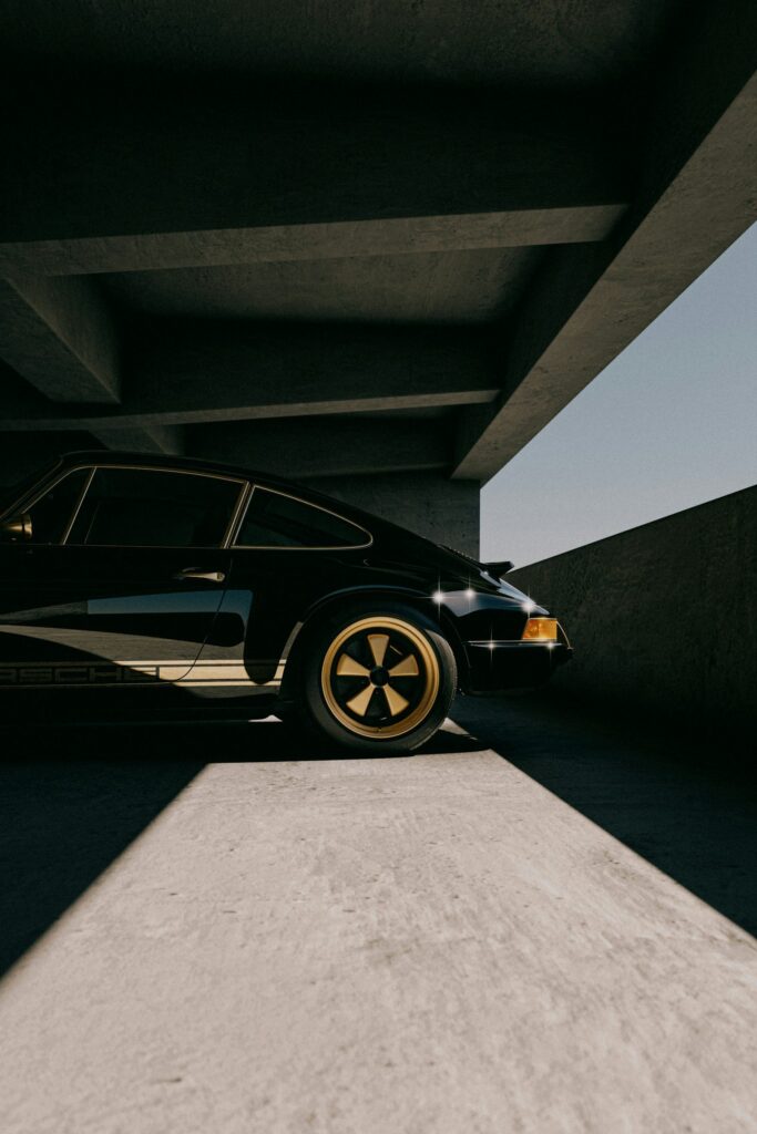 Porsche 911 classique noire à moitié dans l'ombre sous un parking couvert, jantes Fuchs dorées
