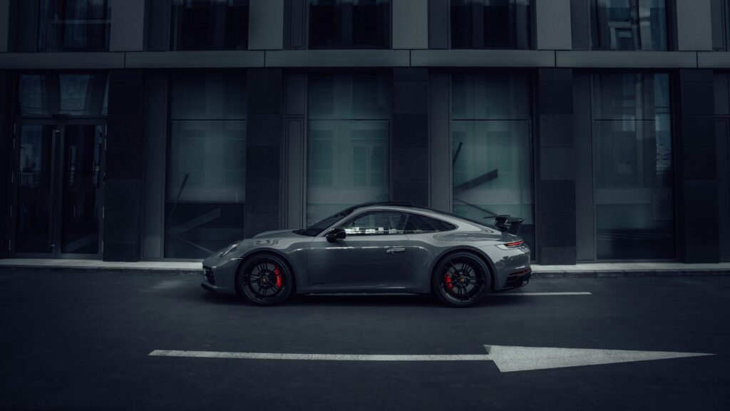 Porsche 911 grise de profil dans une rue sombre aux tons bleutés, flèche au sol