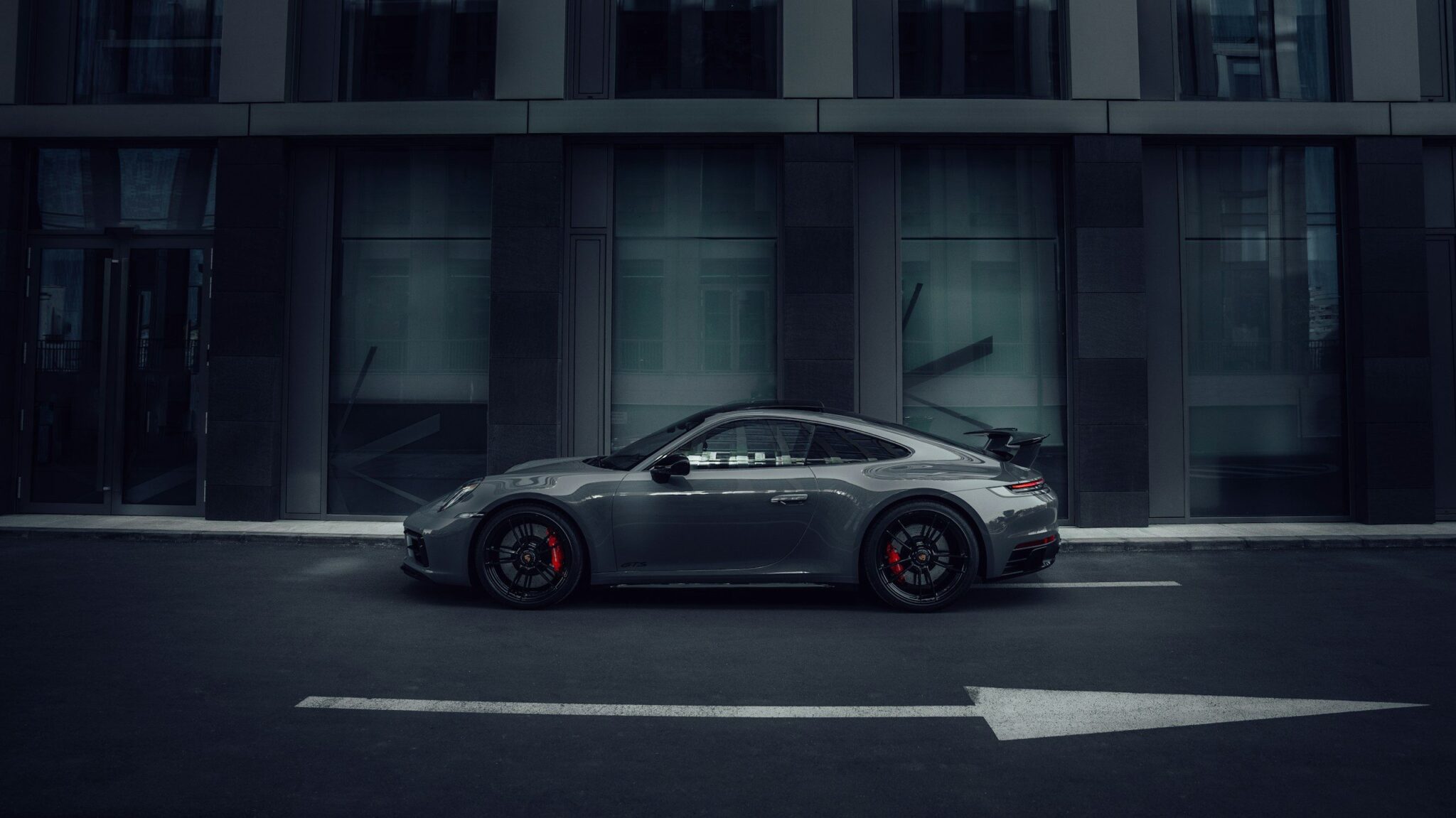 Porsche 911 grise de profil dans une rue sombre aux tons bleutés, flèche au sol