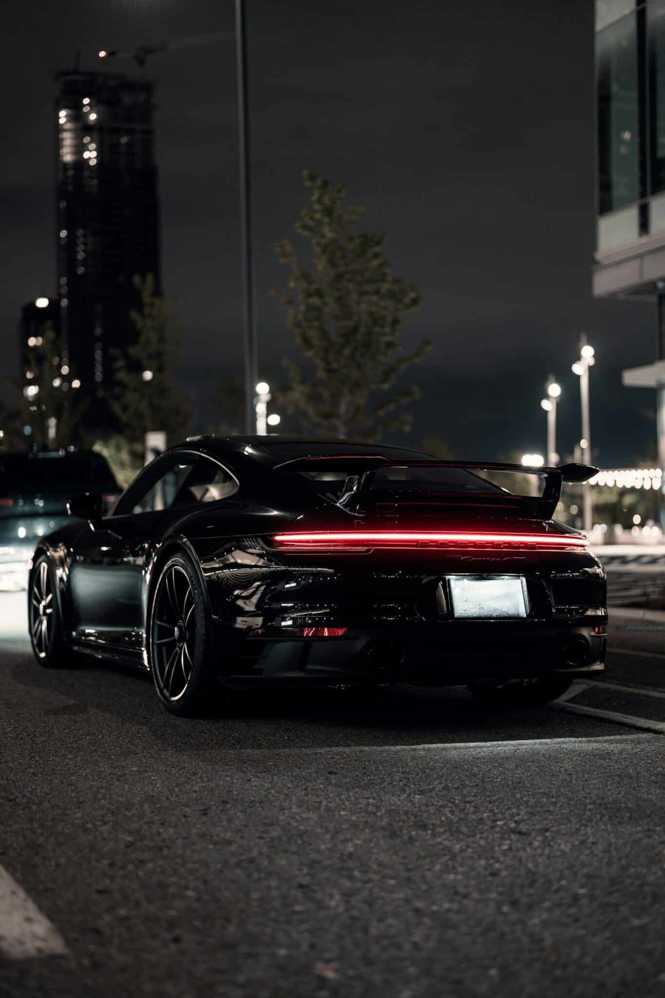 Porsche 911 noire vue de trois quarts arrière, bandeau de feux rouge allumé dans la nuit urbaine