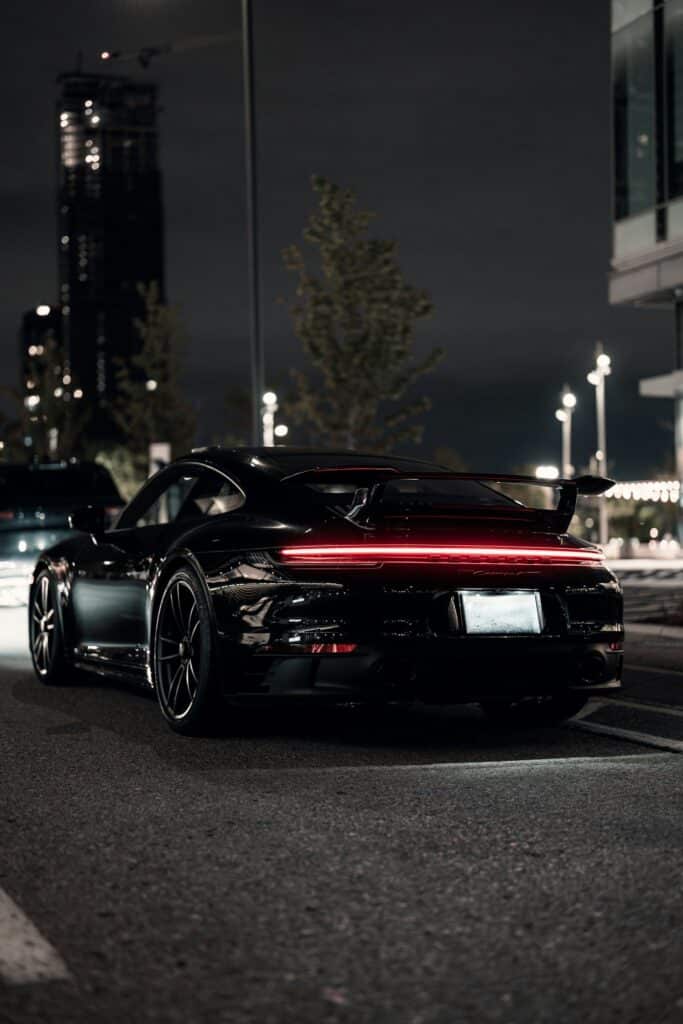 Porsche 911 noire vue de trois quarts arrière, bandeau de feux rouge allumé dans la nuit urbaine