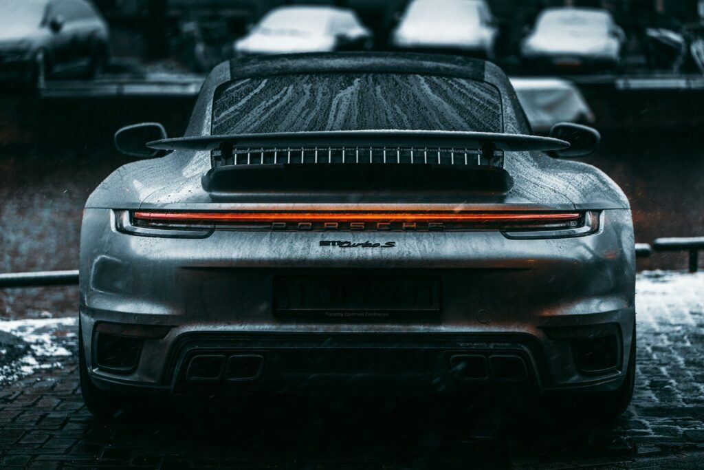 Arrière d'une Porsche 911 Turbo type 992 grise couverte de gouttes de pluie, bandeau lumineux allumé