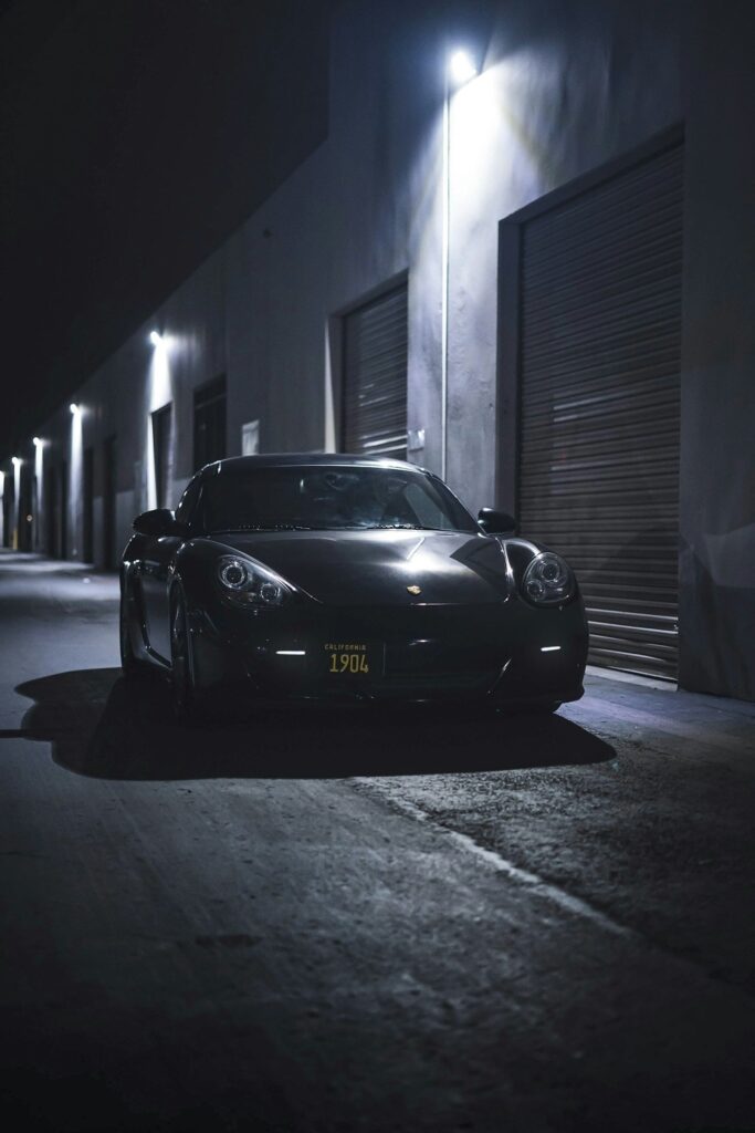 Porsche noire vue de face dans une ruelle sombre éclairée par des appliques murales