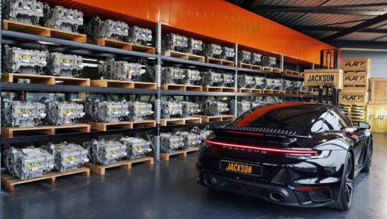 Rayonnages de moteurs flat-six reconditionnés sur palettes et Porsche 911 Turbo noire dans l'entrepôt FLAT